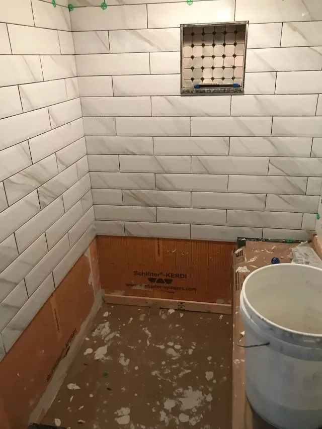 Partially tiled bathroom under renovation with exposed wall section and a bucket on the floor