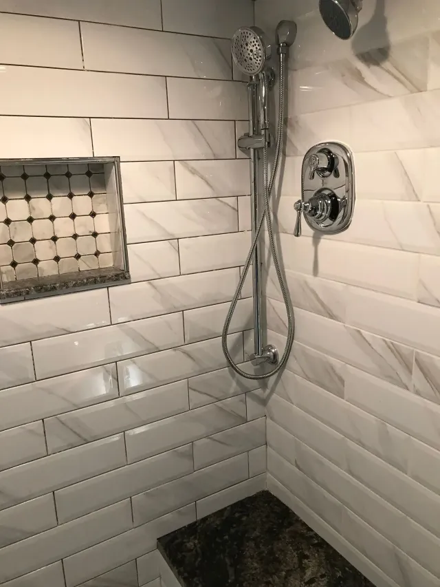 Tiled shower corner with chrome handheld showerhead, wall control, and dark stone shower pan