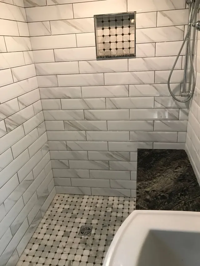 Small tiled shower with a glass block window, wall showerhead, and a built-in shelf.