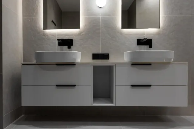Modern bathroom vanity with double sinks, mirrors, and wall-mounted faucets in a gray minimalist interior
