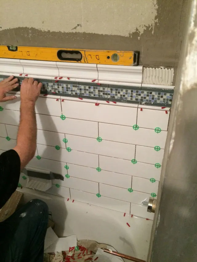 Worker aligning white wall tiles with a level during bathroom tile installation.