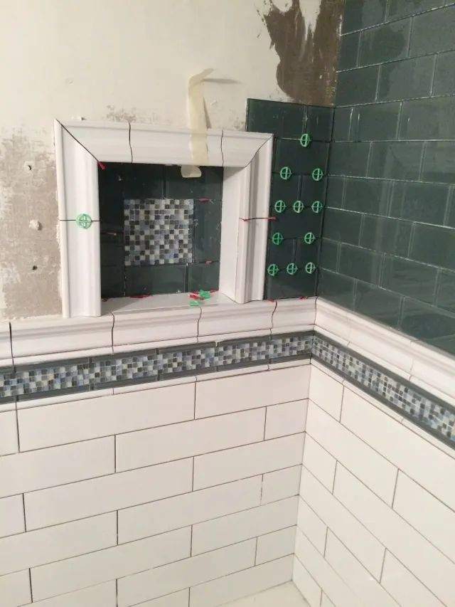 Tiled bathroom shower wall under renovation with exposed black waterproofing and white tile trim