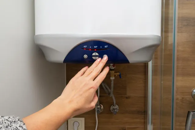 Hand adjusting controls on a wall-mounted water heater in a bathroom.