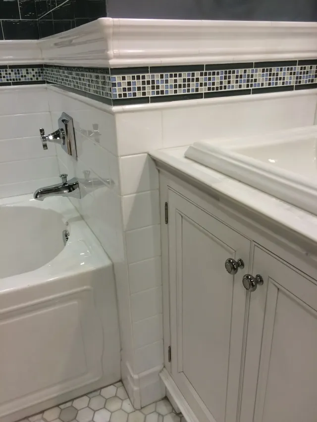 White bathroom tub and sink with decorative tile trim and built-in cabinet