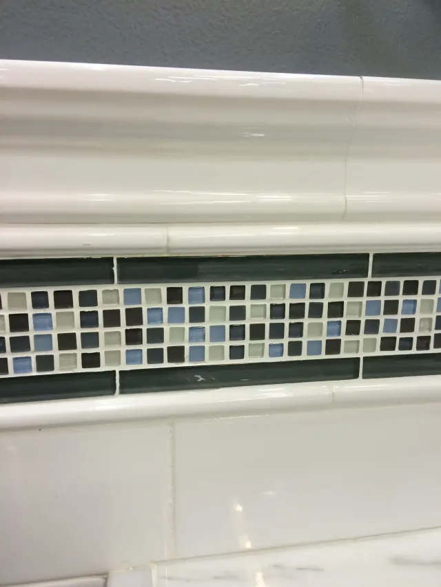 White bathroom tiles with a horizontal band of blue, gray, and black mosaic tiles.
