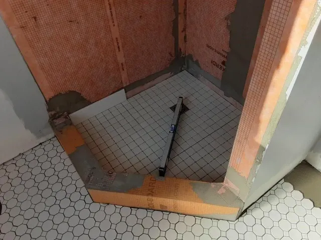 Partially tiled shower area with brick walls and a central drain, seen through a doorway