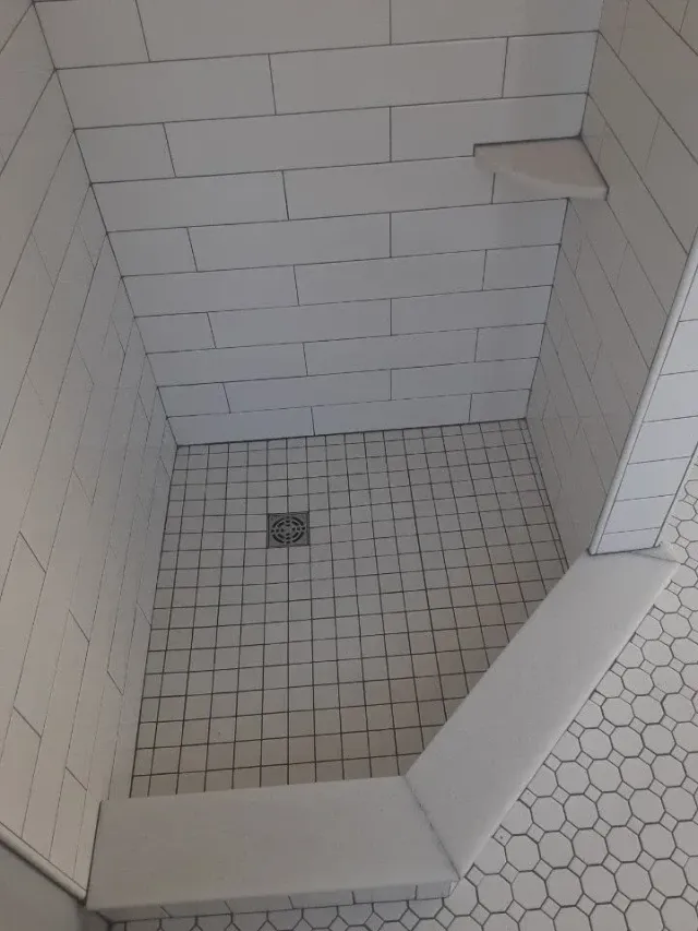 Tiled shower stall with a small square drain and built-in corner shelf.