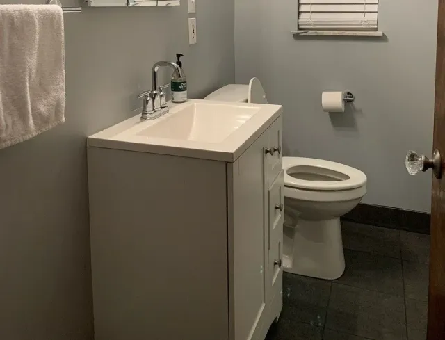 Small bathroom with a white vanity sink, toilet, towel, and dark floor tiles.