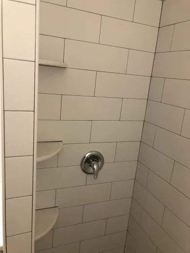 Tiled shower stall under construction with exposed brick walls and a drain in the floor