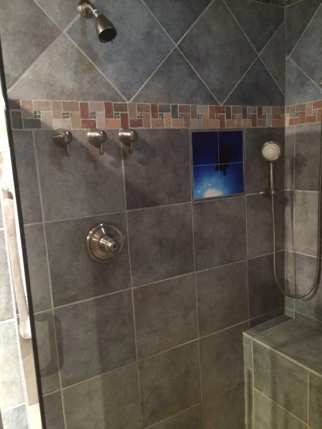 Tiled shower with chrome fixtures, mosaic border, wall niche, and handheld showerhead