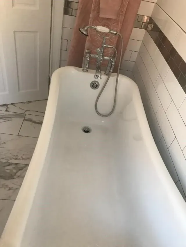 Clawfoot bathtub in a small tiled bathroom with a chrome faucet and handheld showerhead
