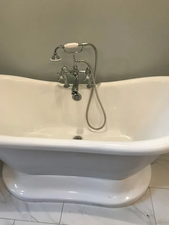 White freestanding bathtub with chrome faucet and handheld shower against a beige wall