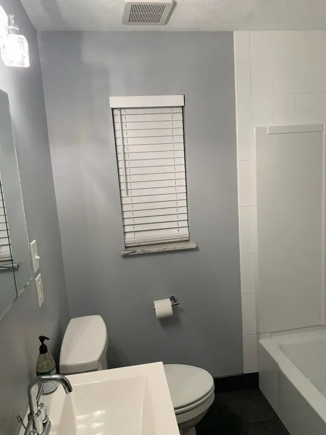 Small bathroom with a toilet, window blinds, bathtub, and gray walls.