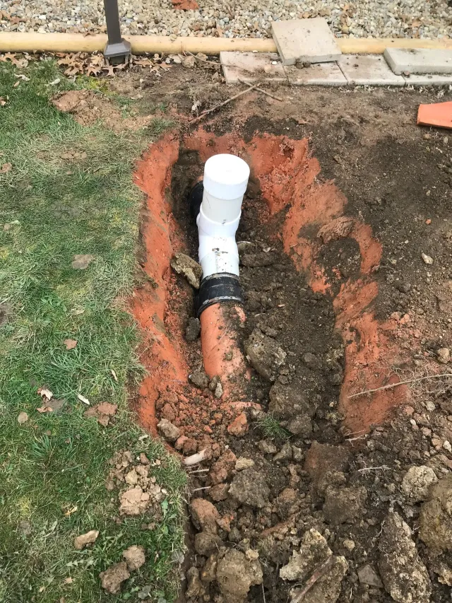 Trenched PVC pipe repair in a yard, with exposed dirt and a white elbow fitting.