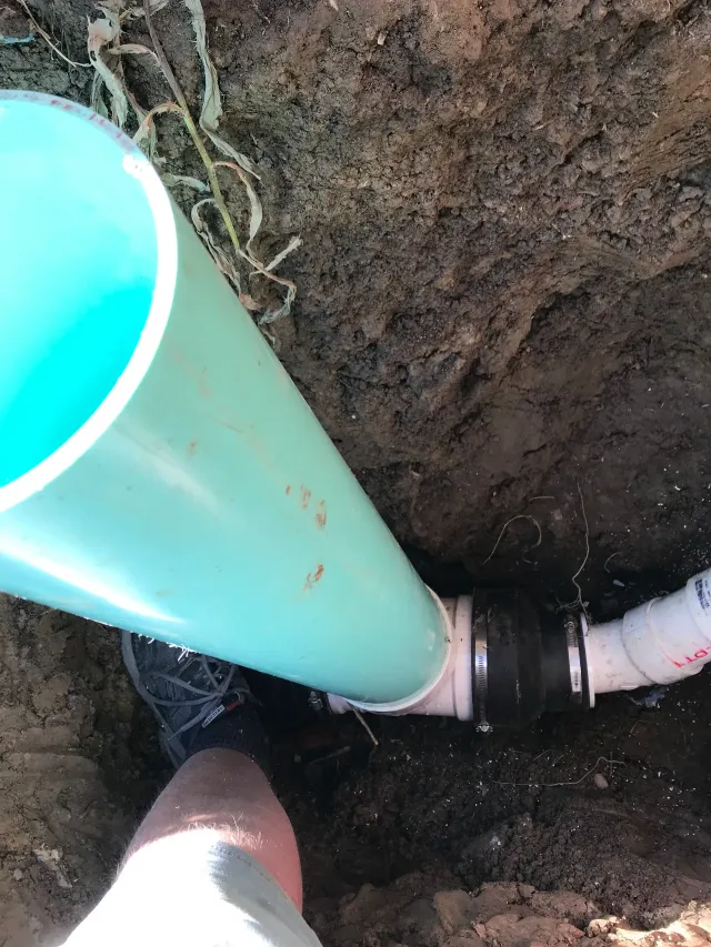 Blue pipe connected to a white pipe in a dirt trench, viewed close up.