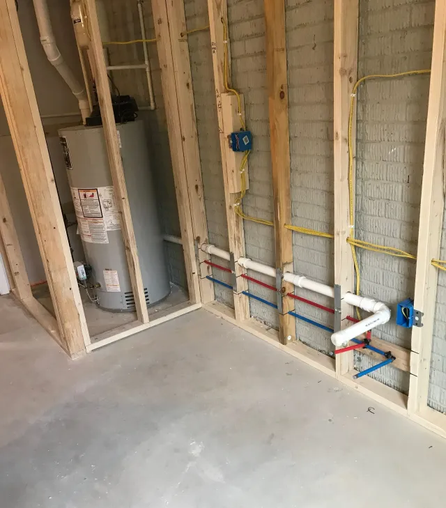 Unfinished bathroom framing with exposed plumbing, gray water heater, and concrete floor